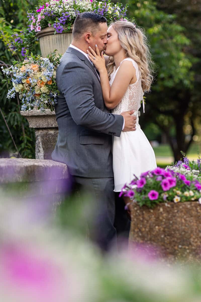 Elopement bride and groom hug as they stand next to pink and purple flowers in shade during sunset